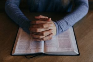 Person reading the Bible with their hands together in prayer